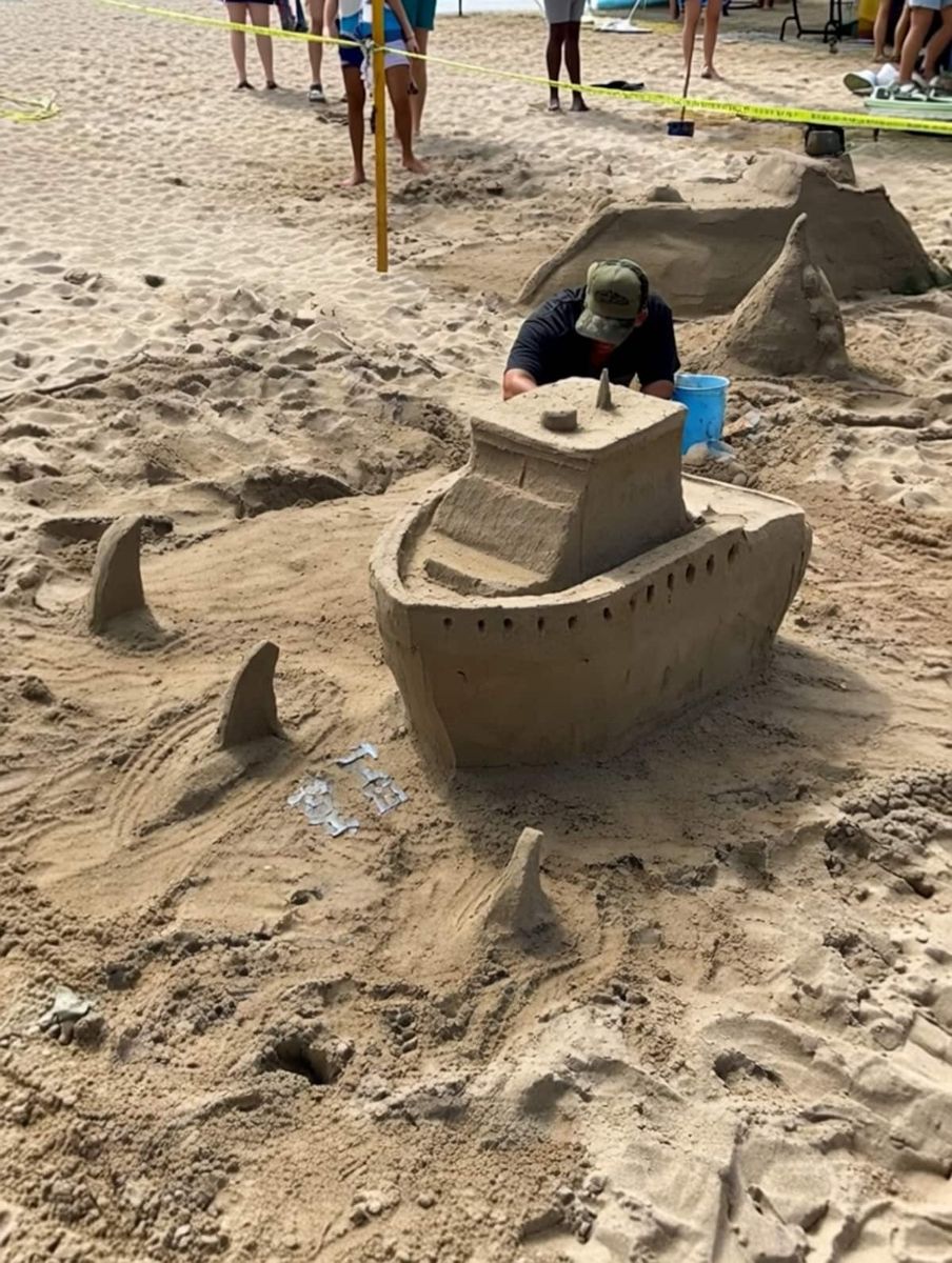 Sand sculpture of a boat surrounded by shark fins