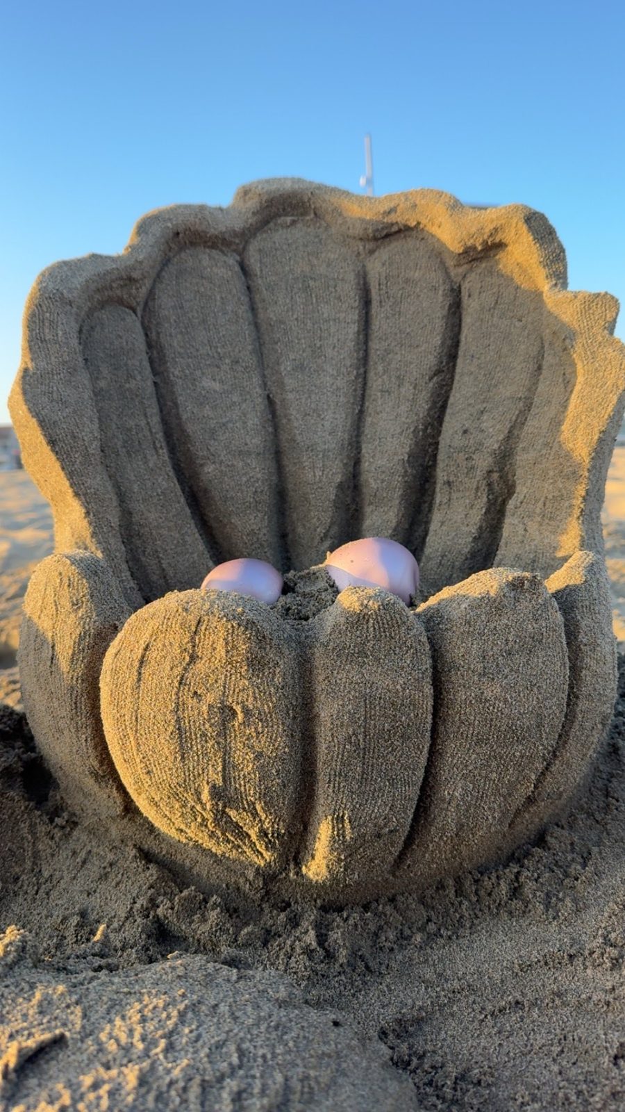 Giant clam shell sand sculpture holding two pearls at sunset