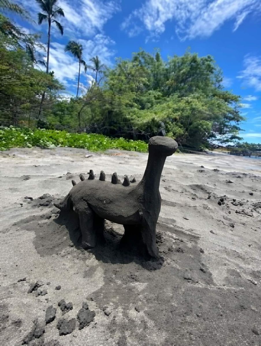 Dinosaur sand sculpture under palm trees