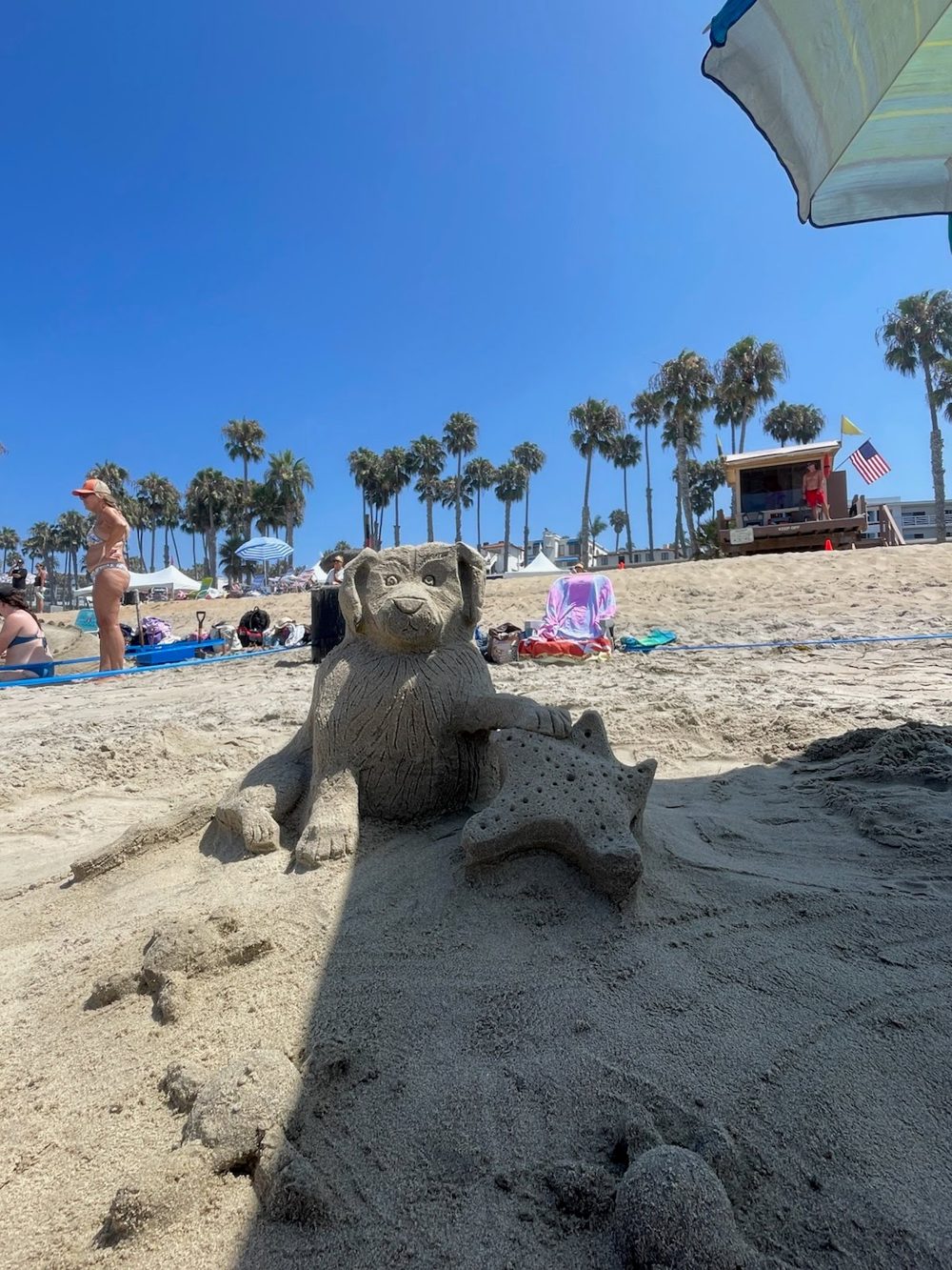 Sand sculpture of a puppy holding a starfish on the beach by a lifeguard tower