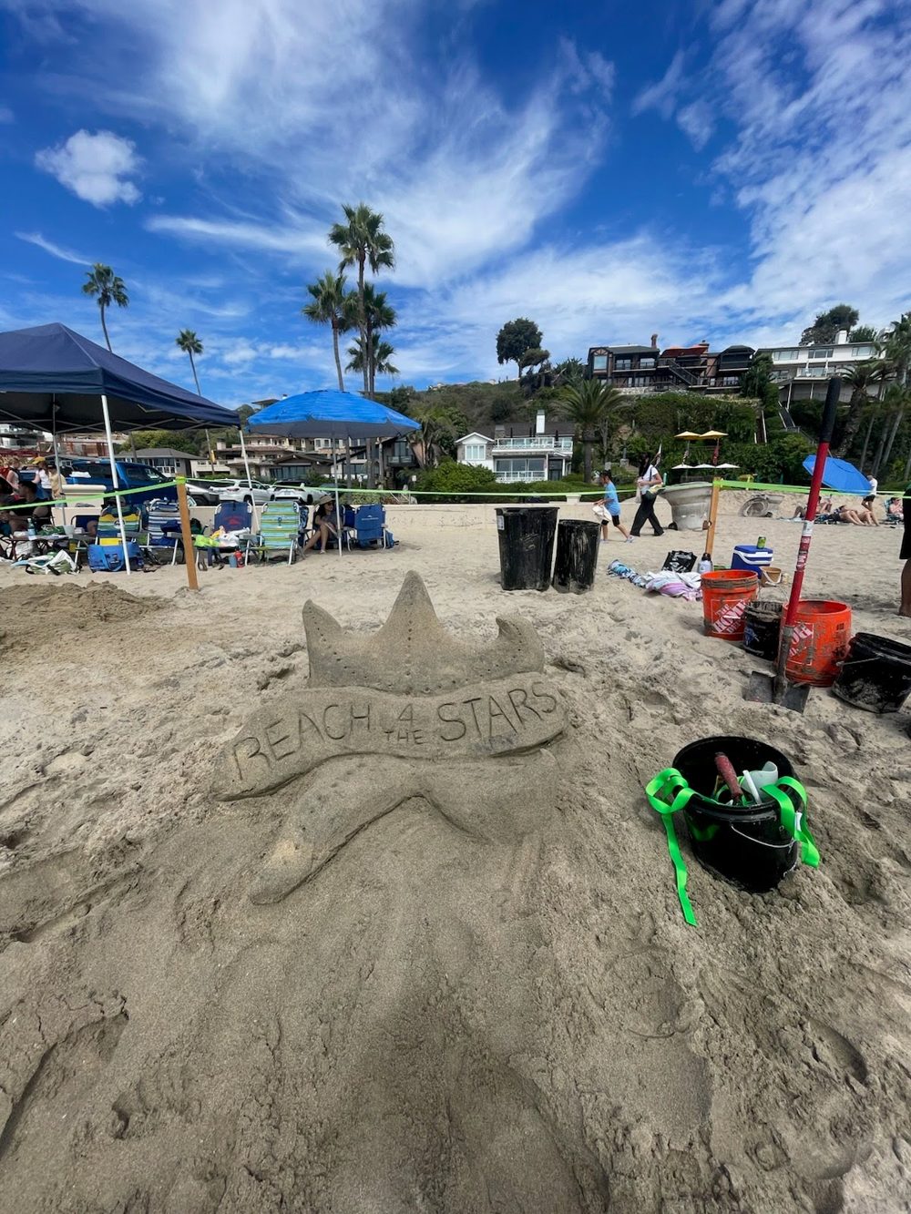 Sand crown sculpture carved with Reach 4 the Stars on a busy beach