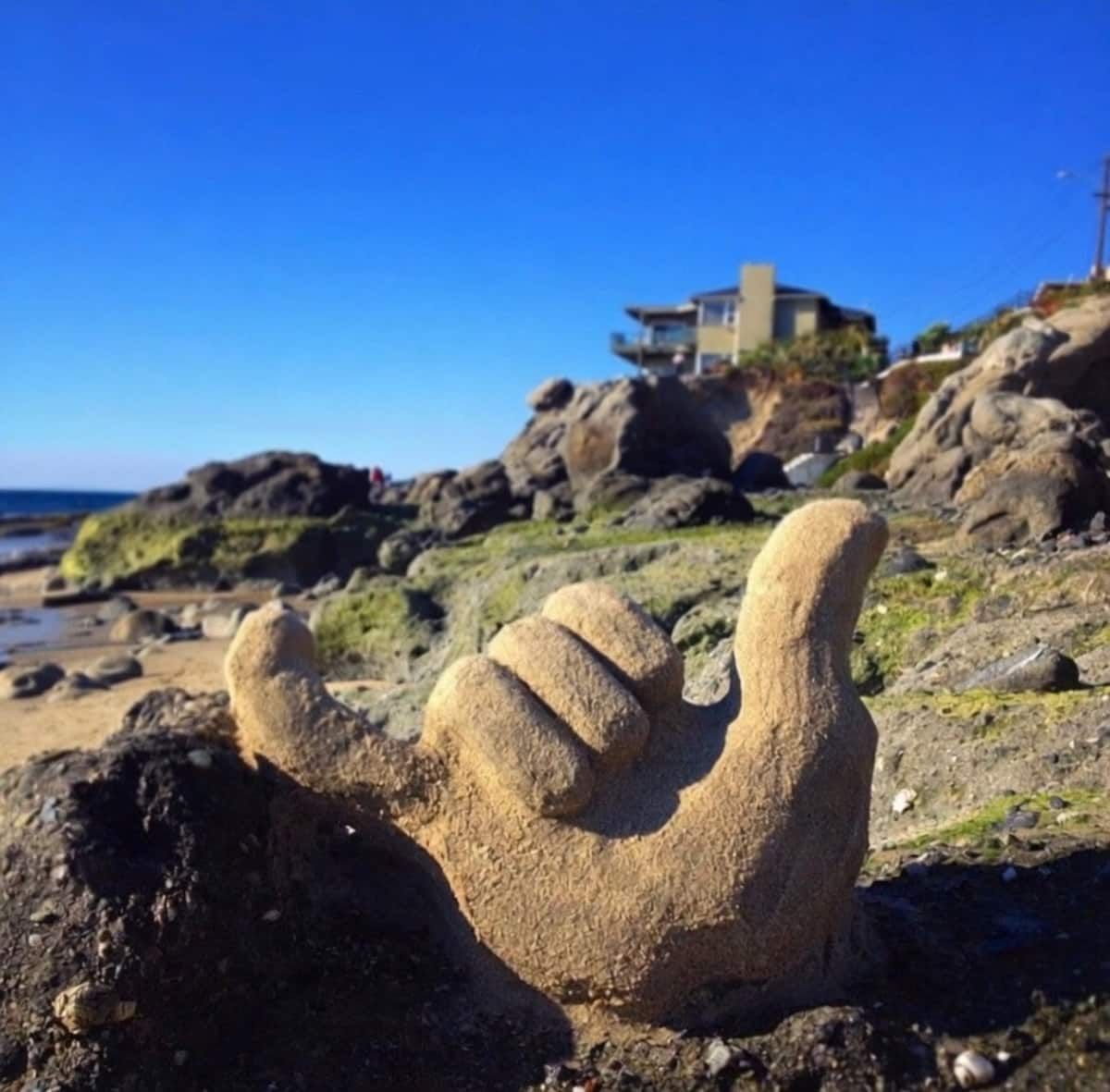 Sand sculpture of a shaka hand on the rocks by the ocean
