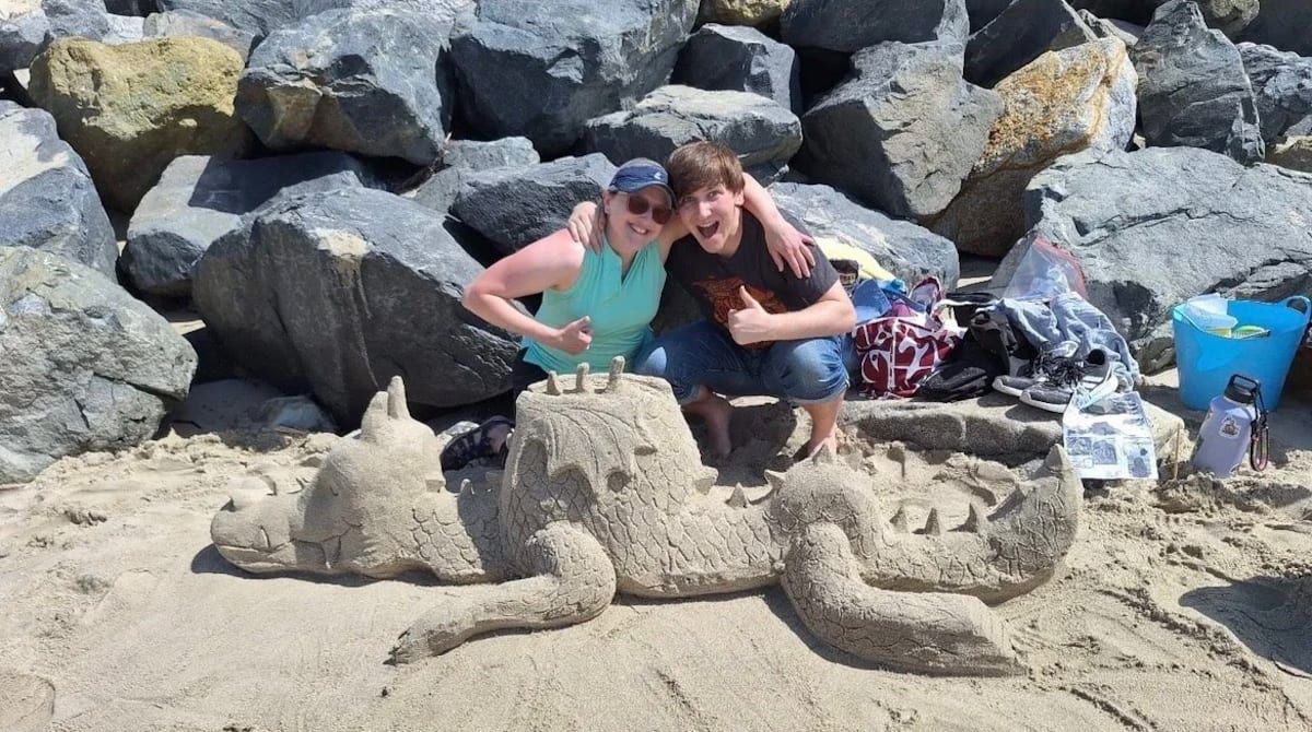 Two guests smiling behind a sand dragon sculpture